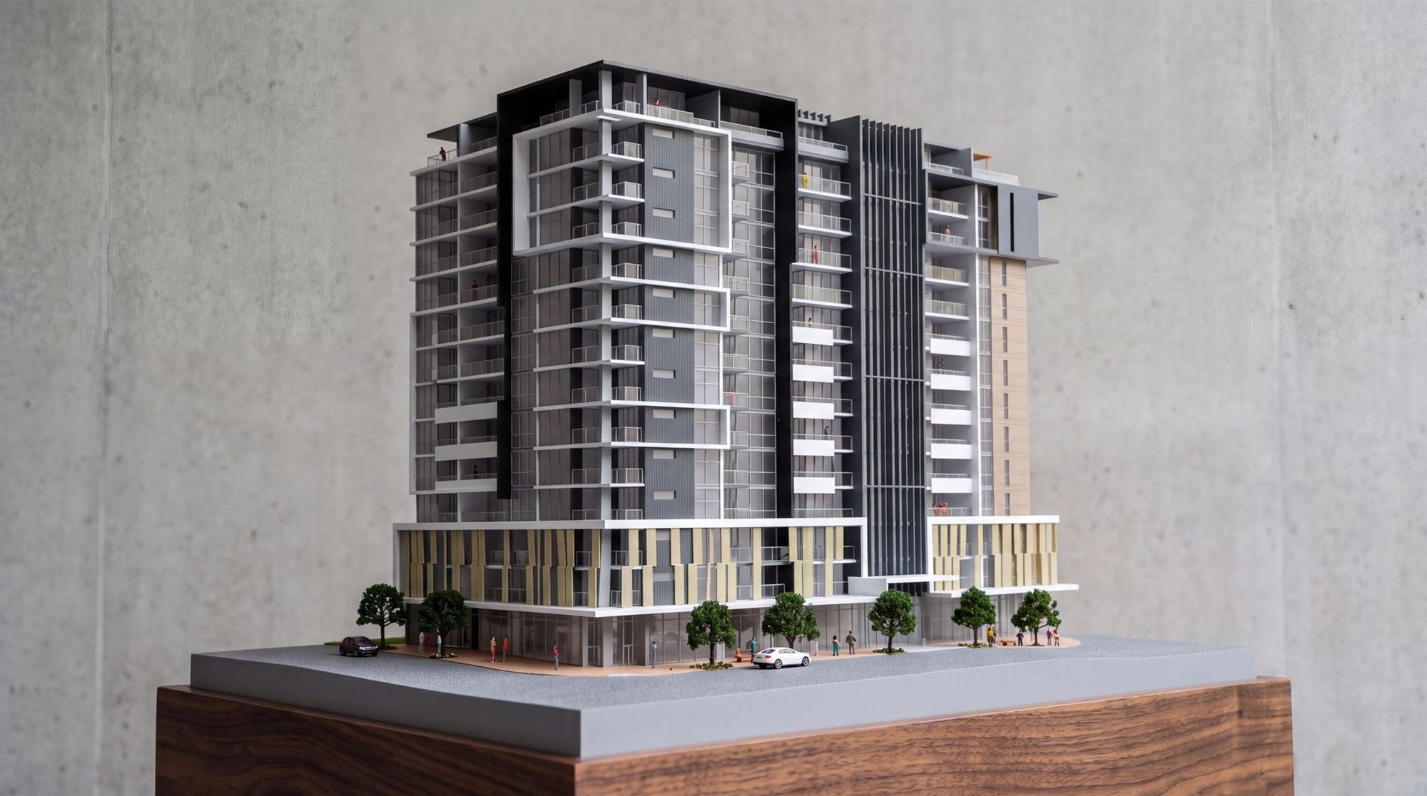 Photograph of the hand-built scale model of a residential tower, on its plinth against a concrete wall
