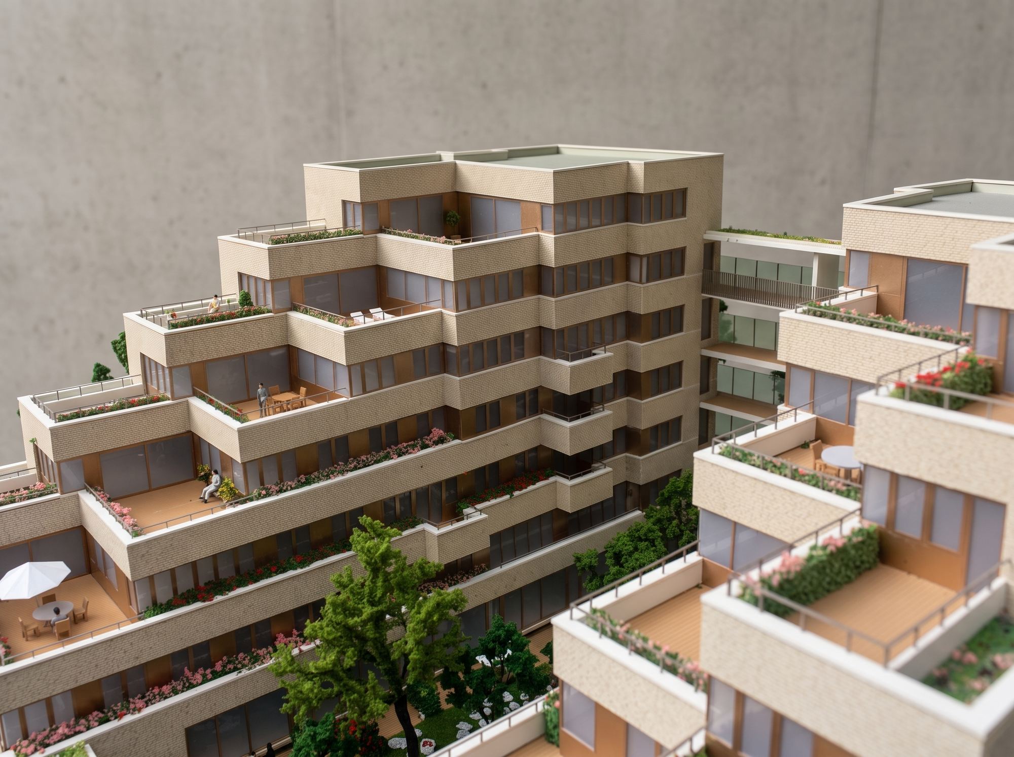 Detail van een maquette van terrasvormige appartementen: lichte baksteen, dakterrassen met bloeiende plantenbakken, meubels, figuren en bomen in de binnentuin